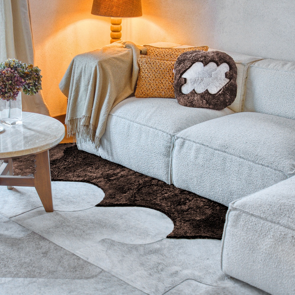 Coussin marron sur canapé blanc confortable, et tapis marron en peau lainée et peau de vache.