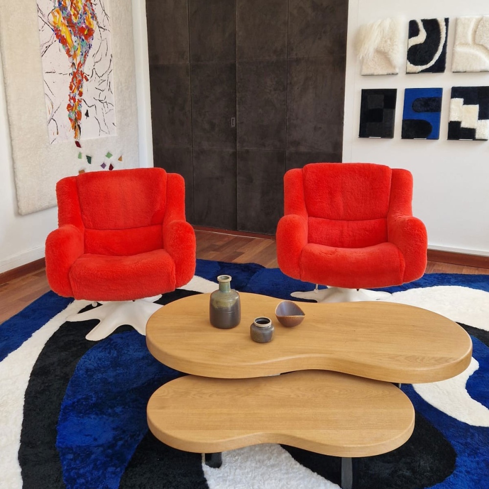 Vases and bowl on a coffee table next to two red armchairs.