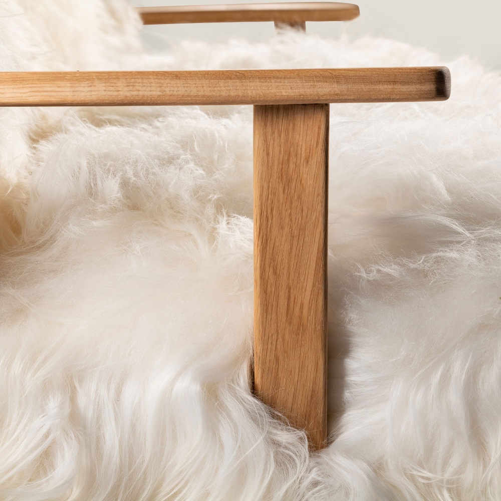 Des accoudoirs en chêne massif complètent une assise en mouton islandais poils longs blanc naturel. Un mobilier signé Norki.