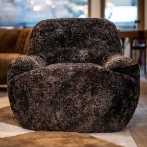 Dark-brown armchair upholstered in dark-brown curly shearling and set on a metal swivel system, furniture made in France.