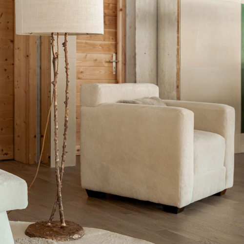 Luxurious white skin cube armchair decorates the living room of a modern chalet with a bronze lamp and a white carpet.