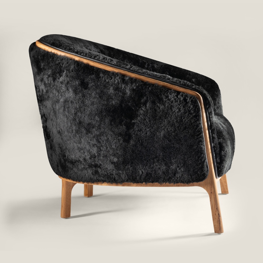 A very comfortable armchair with a rounded backrest upholstered in black lambskin to decorate your home with elegance.