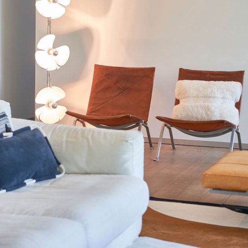 Salon décoré avec une paire de fauteuils vintages de Poul Kjaerholm, un coussin en mouton blanc et une lampe moderne en métal