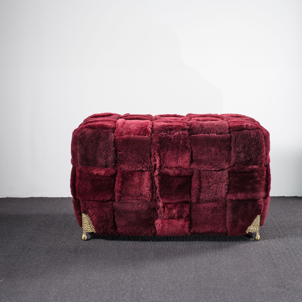 Un grand pouf bordeaux en peau lainée et pieds en laiton dans une décoration moderne et élégante.