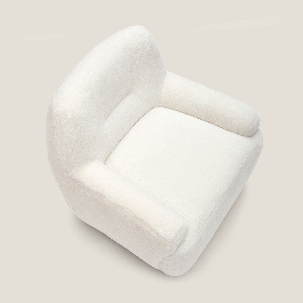 Fauteuil avec assise large et confortable en peau lainée blanche et accoudoirs larges, pour un coin lecture dans votre salon.