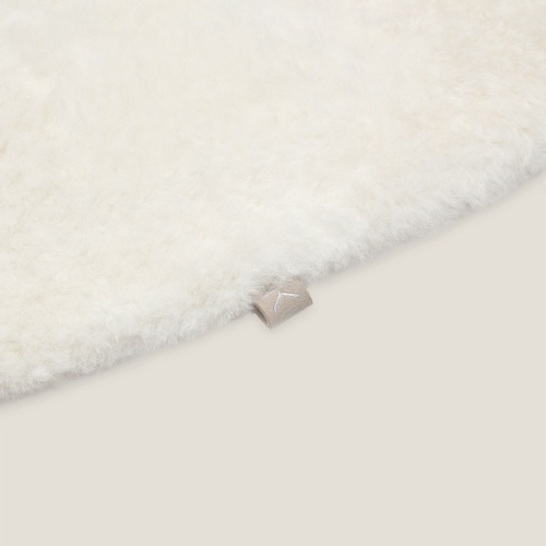 Détail du Tapis Icicle rond en peau lainée et de son étiquette avec le monogramme contemporain NK Norki.