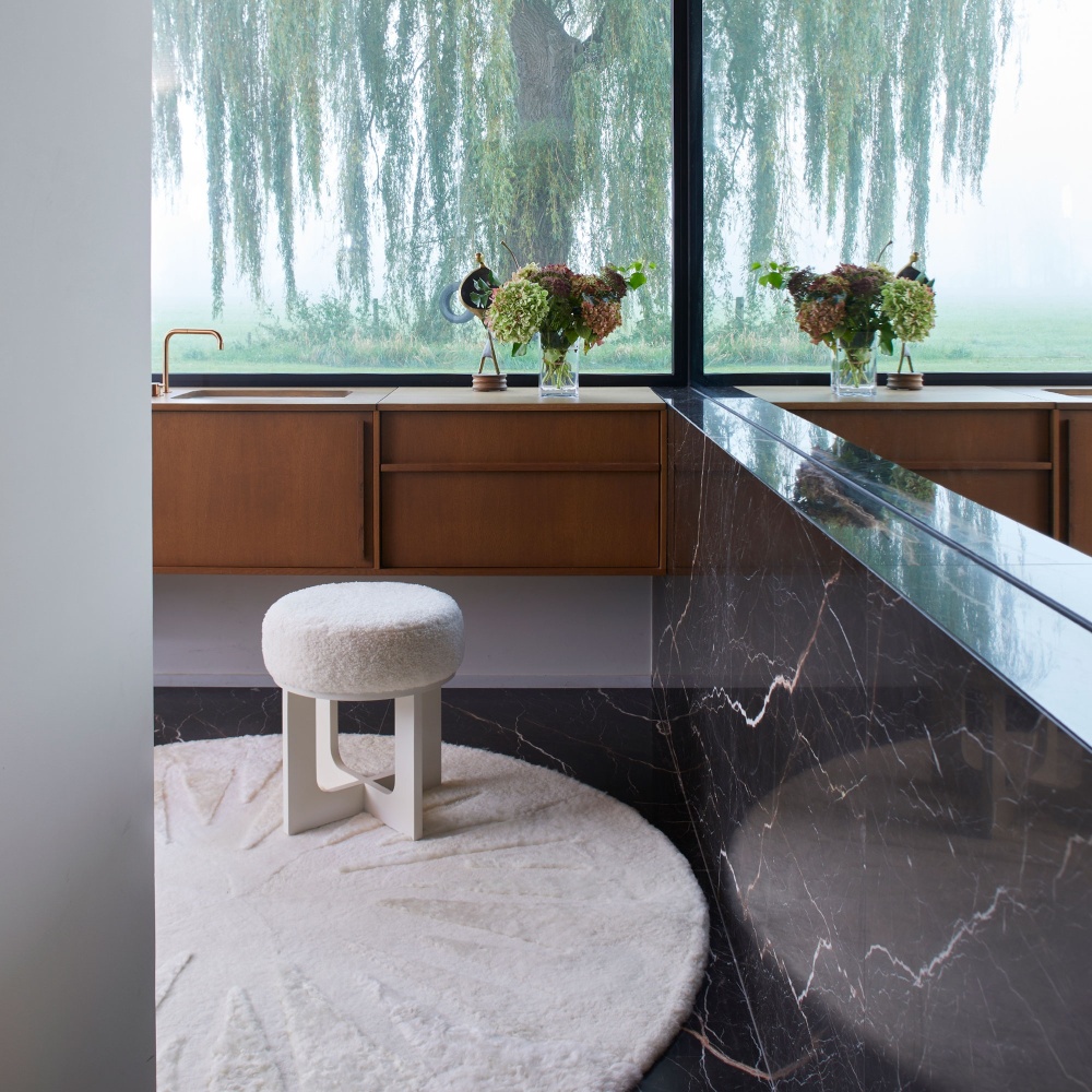 Round white designer carpet in a contemporary bathroom in black marble and white Tea Time stool by Norki.