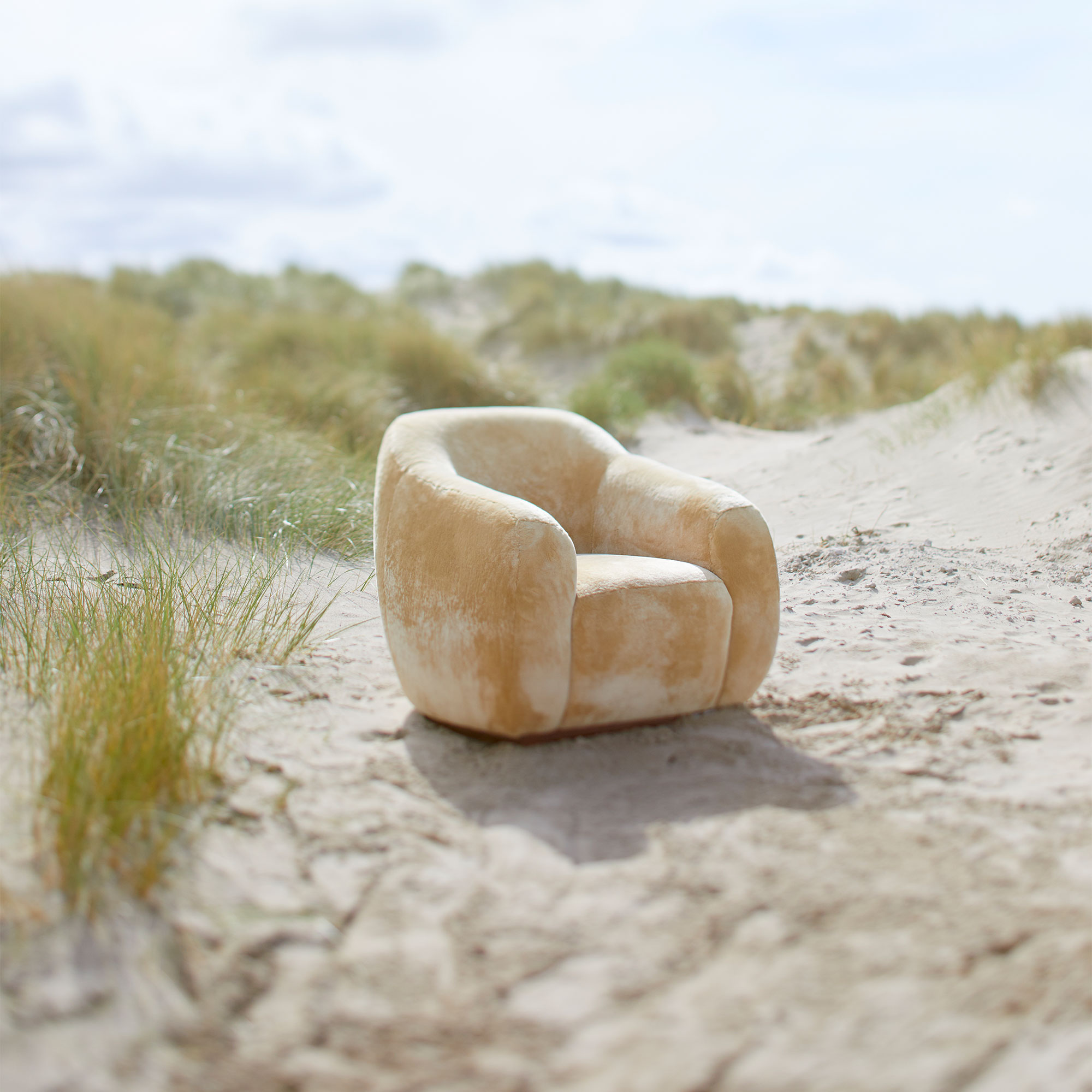 Fauteuil coco beige sur une plage de sable en pleine nature.